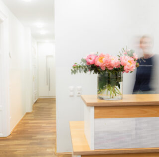 Heller Empfangsbereich mit Holztresen und rosa Pfingstrosen in Glasvase