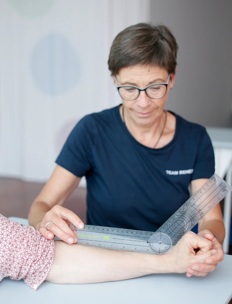 barbara-dopfer-handtherapie-behandlung-praxis-benedikt-muenchen Barbara Dopfer, zertifizierte Handtherapeutin der Praxis Benedikt München, misst den Bewegungswinkel am Arm einer Patientin