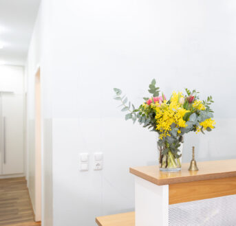 Heller Empfangsbereich der Praxis Benedikt München mit Holztresen und buntem Blumenstrauß in Glasvase