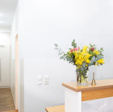 empfang-praxis-benedikt-muenchen-blumen-tresen Heller Empfangsbereich der Praxis Benedikt München mit Holztresen und buntem Blumenstrauß in Glasvase