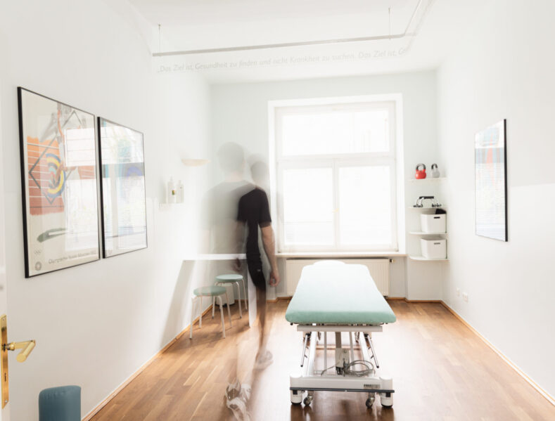 Heller Behandlungsraum der Physiotherapie Praxis Benedikt München mit Behandlungsliege, Holzboden und inspirierendem Zitat an der Wand