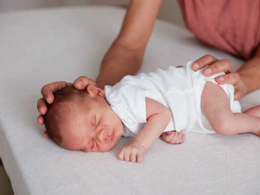 Osteopathin legt die Hände sanft an Kopf und Becken eines schlafenden Babys – Kinderosteopathie in München